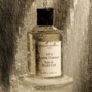 Botella de perfume Thomas Kosmala No. 4 Après l'Amour Eau de Parfum, con un diseño clásico, parcialmente cubierta de gotas de agua que escurren, sobre una base húmeda y un fondo de lentejuelas brillantes.